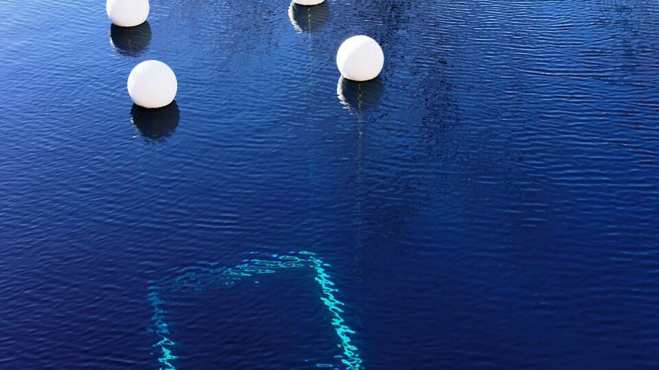 Four white spherical objects floating on a body of water with ripples.