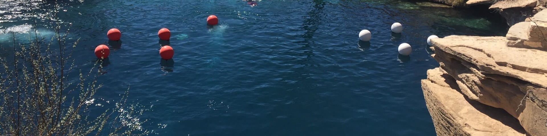 A clear blue pool with red and white floating balls, surrounded by stone walls and trees.