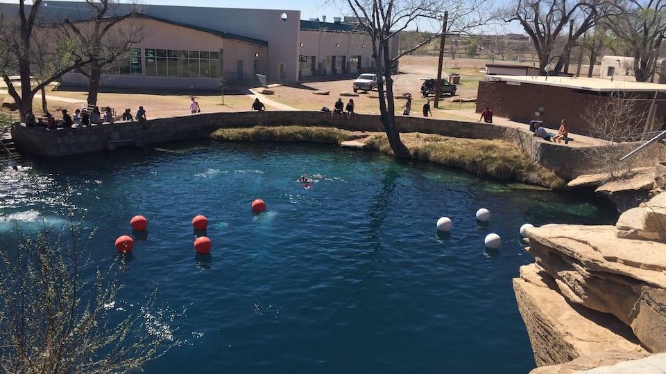 A clear blue pool with red and white floating balls, surrounded by stone walls and trees.