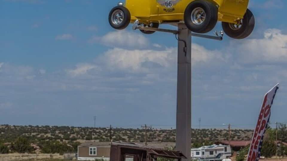 A yellow vintage car suspended on a truck in a desert landscape.