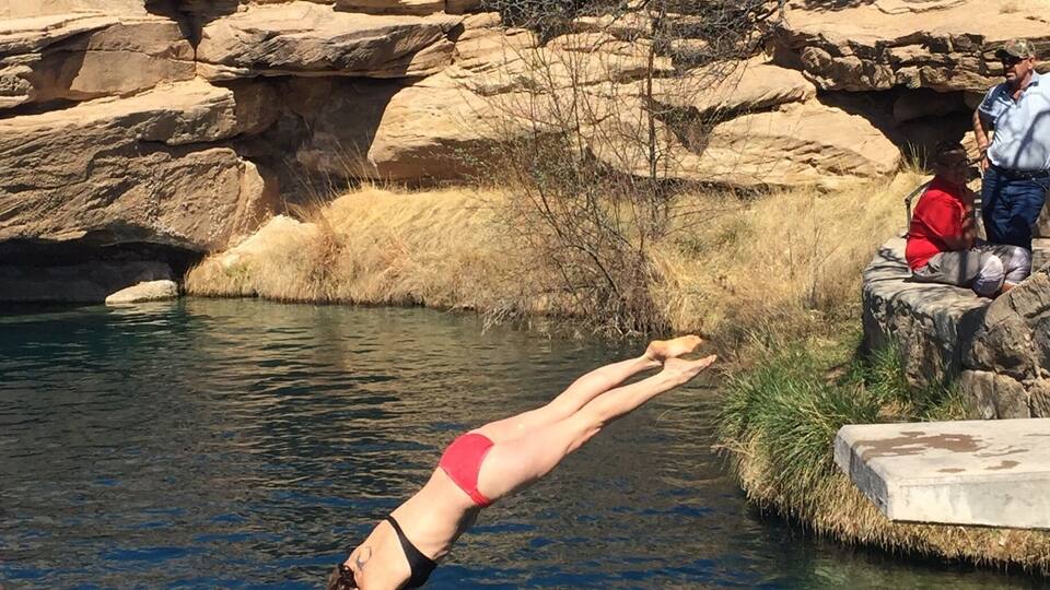 A person diving into a clear pool surrounded by rocky terrain and sparse vegetation.