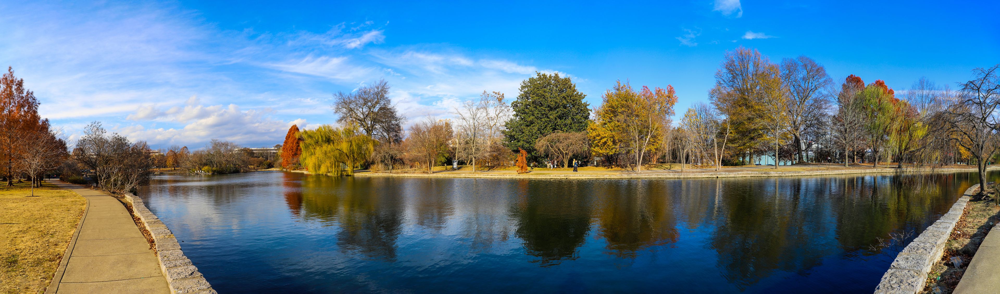 a stunning panoramic shot of the blue waters of the lake in the park surrounded by gorgeous autumn colored trees reflecting off the lake with blue sky at Centennial Park in Nashville Tennessee USA