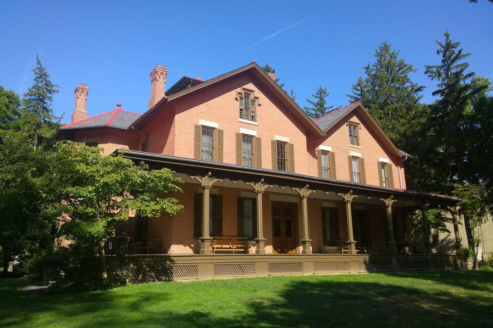 Une grande maison en briques avec un toit rouge, un porche à colonnes et une cheminée.