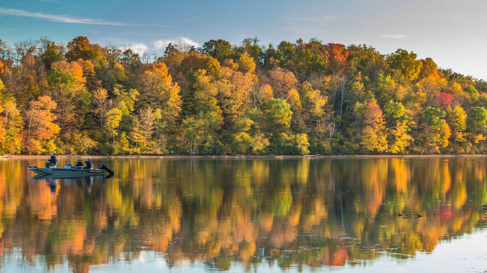 A calm lake with a reflection of autumn trees and a small boat with people.