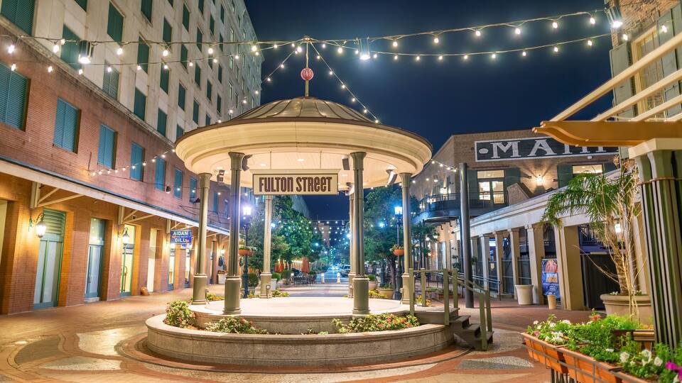A well-lit plaza with a central gazebo, surrounded by brick buildings and string lights.