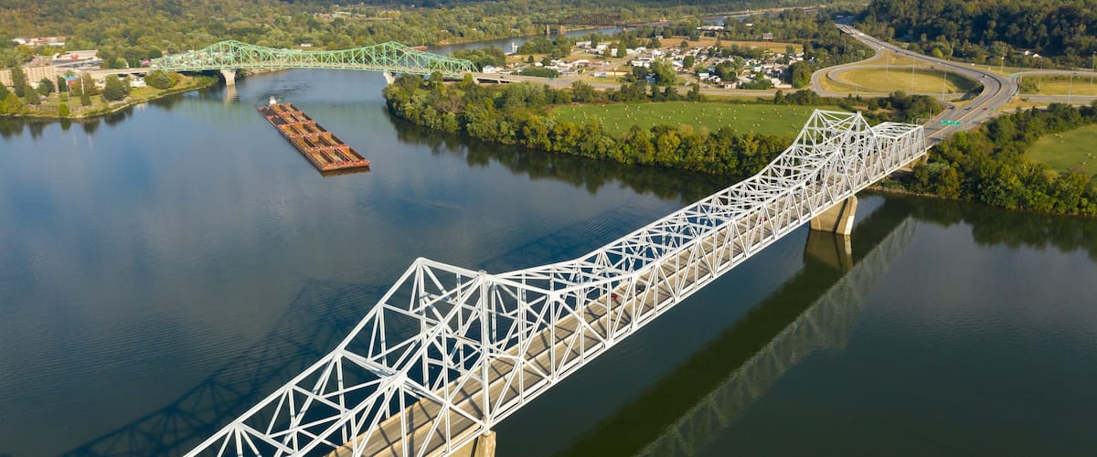 A steel bridge over a river, surrounded by greenery and a small town.