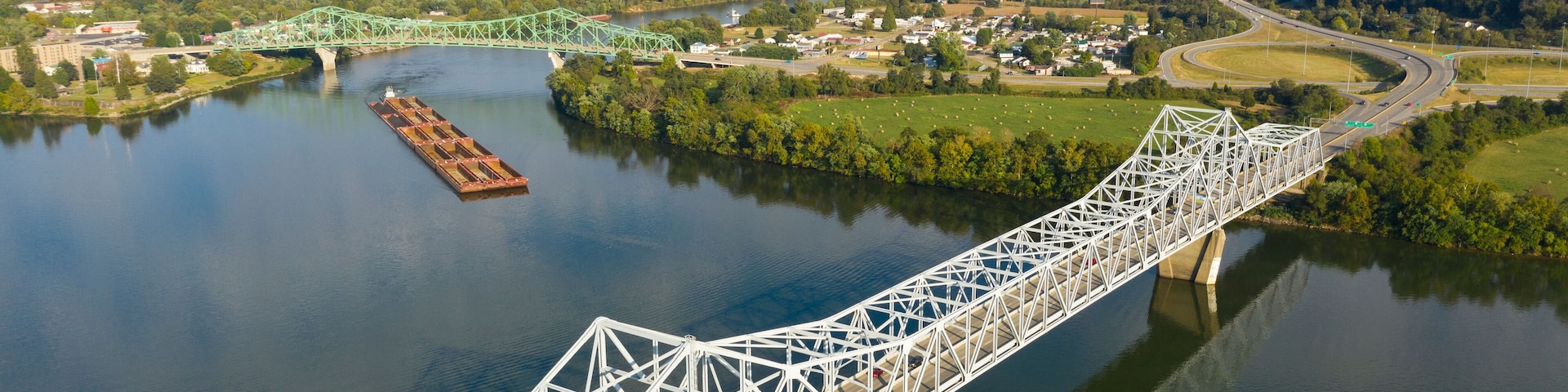 A steel bridge over a river, surrounded by greenery and a small town.