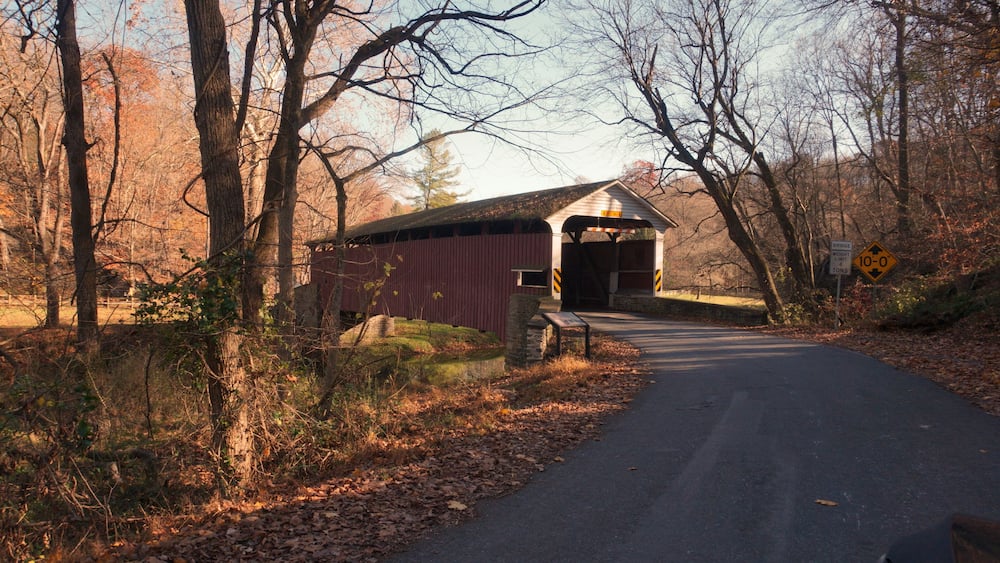 A covered bridge in a wooded area with a sign indicating a weight limit of 10-0 tons.