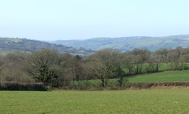 A rural landscape with rolling hills, scattered trees, and a clear sky.