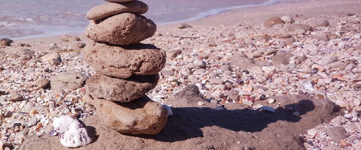 A stack of smooth stones on a pebbly beach with the ocean in the background.
