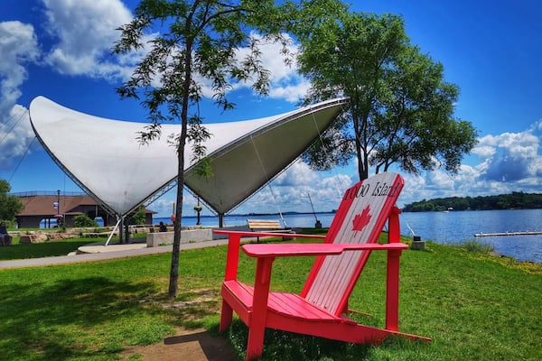 A red chair with a '1000 Islands' sign, a white canopy structure, and a lake with a dock in the background.