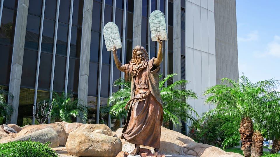 A statue of a figure holding tablets in front of a modern building.