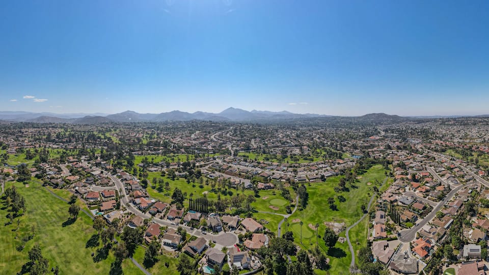 A panoramic view of a suburban area with a golf course, residential neighborhoods, and distant mountains under a clear sky.