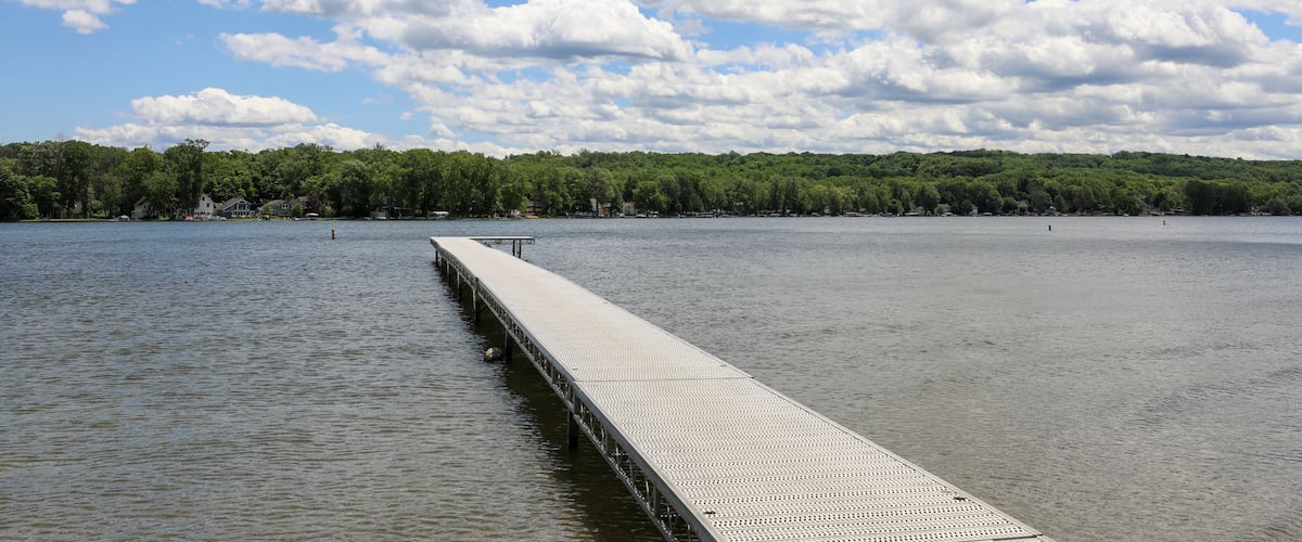 A long pier extending into a calm lake, surrounded by a forested shoreline under a partly cloudy sky.