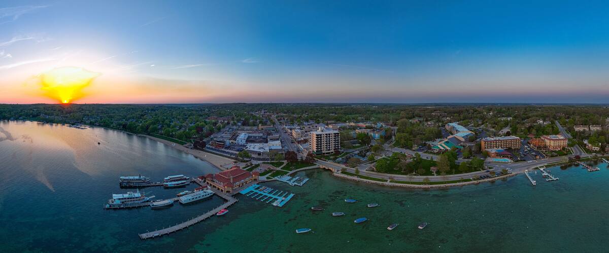 Une vue d’une ville côtière au coucher du soleil, avec un port de plaisance, des bateaux et des bâtiments.
