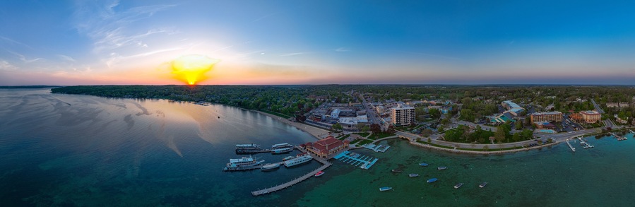 Paisagem urbana costeira ao pôr do sol, com um porto, barcos e edifícios.