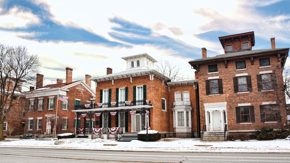 A historic brick building with a white facade and green shutters, adorned with American flags and patriotic decorations.