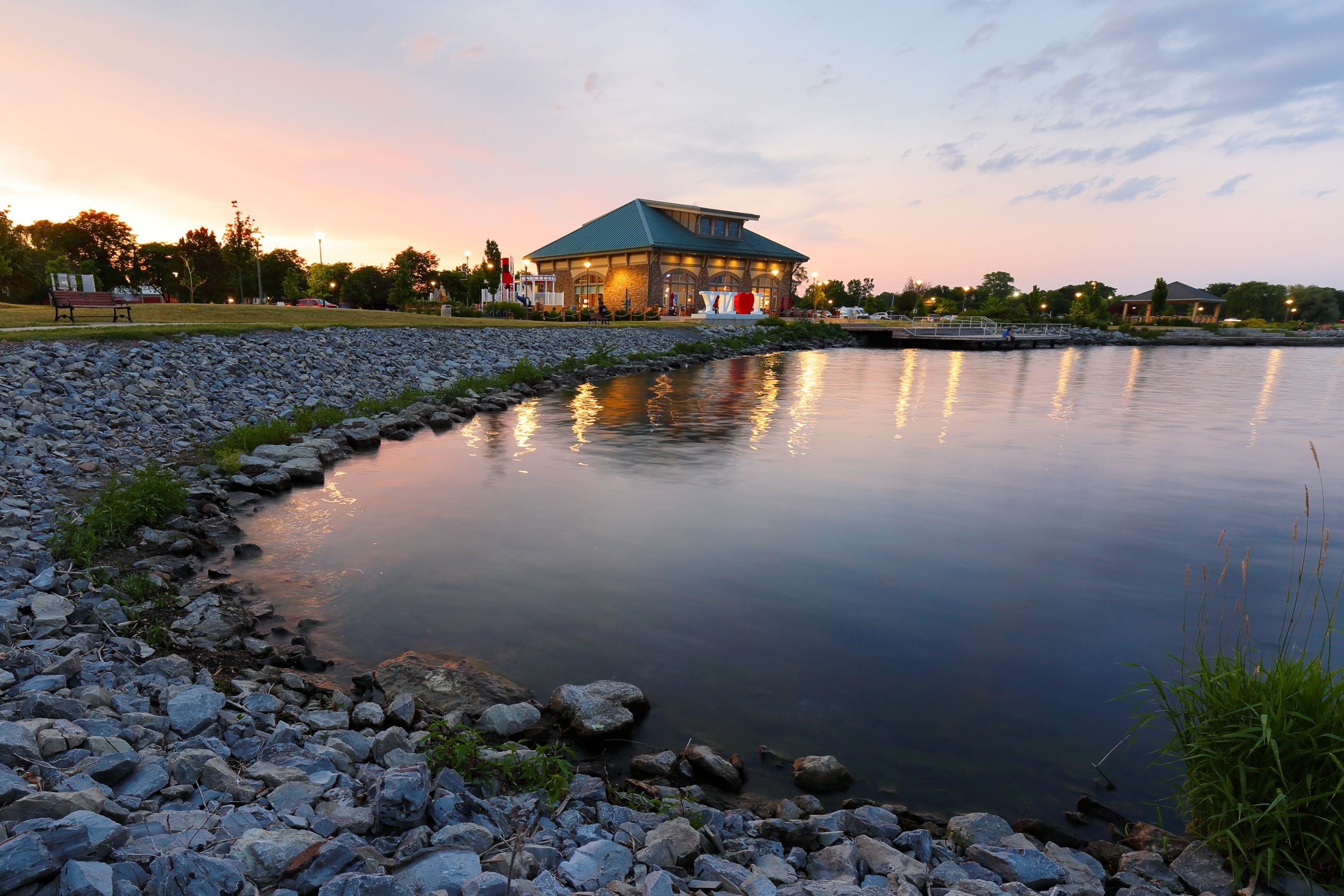 A lakeside view with a gazebo, a rocky shoreline, and a sunset.