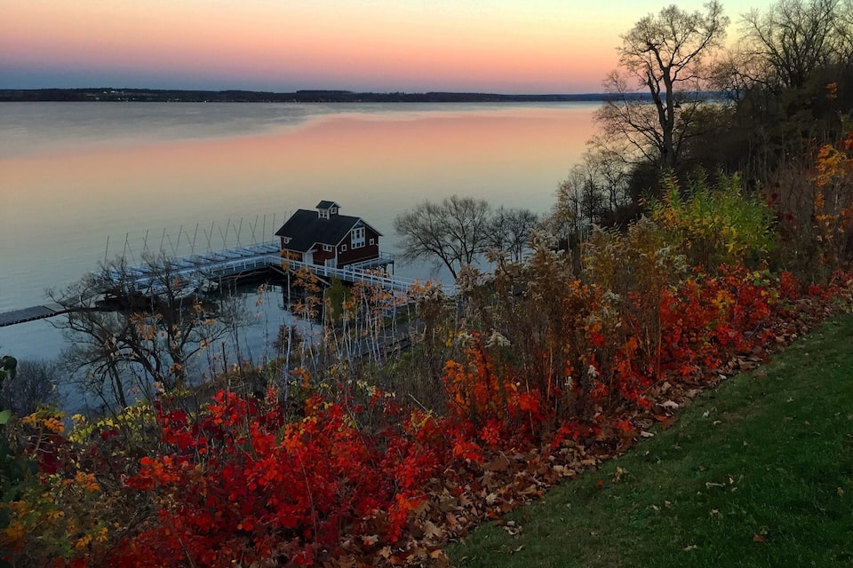 A house on a dock by a calm lake with autumn foliage.