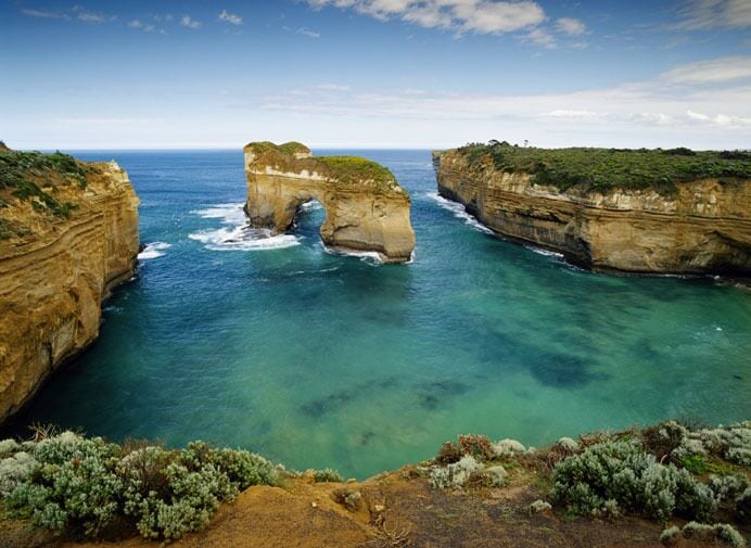 A coastal landscape with a natural rock arch formation and clear blue waters.