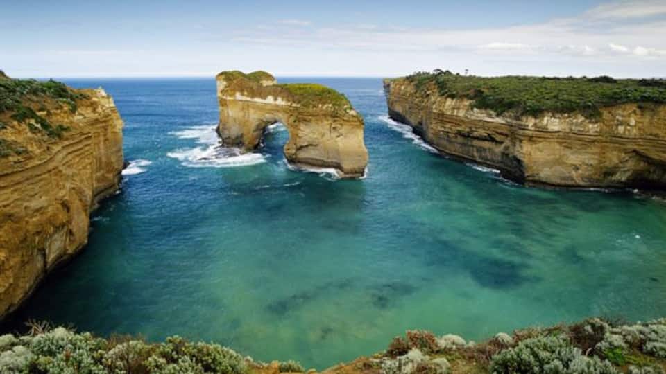 A coastal landscape with a natural rock arch formation and clear blue waters.