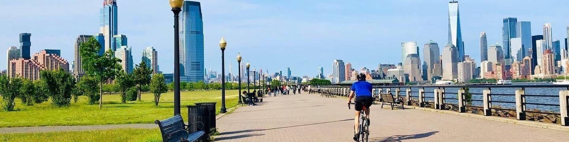 A paved walkway with benches, a cyclist, and a city skyline in the background.