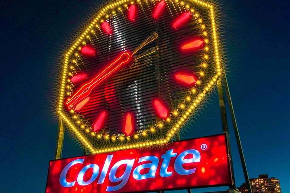 A large illuminated clock with a Colgate sign below it.