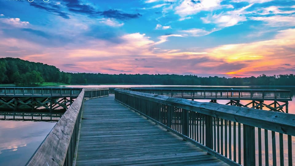 A wooden pier extending into a body of water with a sunset sky.