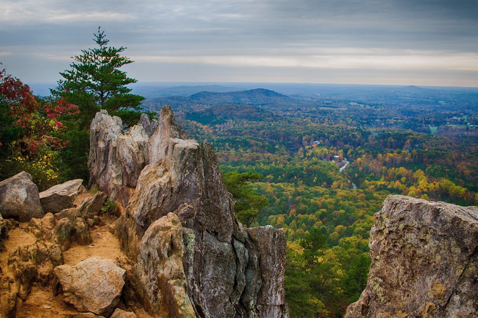 A rocky terrain with a view of a forested valley and distant mountains.