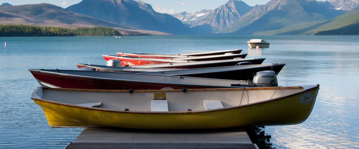 A row of boats docked at a pier with a mountain range in the background.