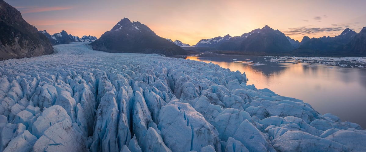 A glacier with ice formations and mountains in the background.