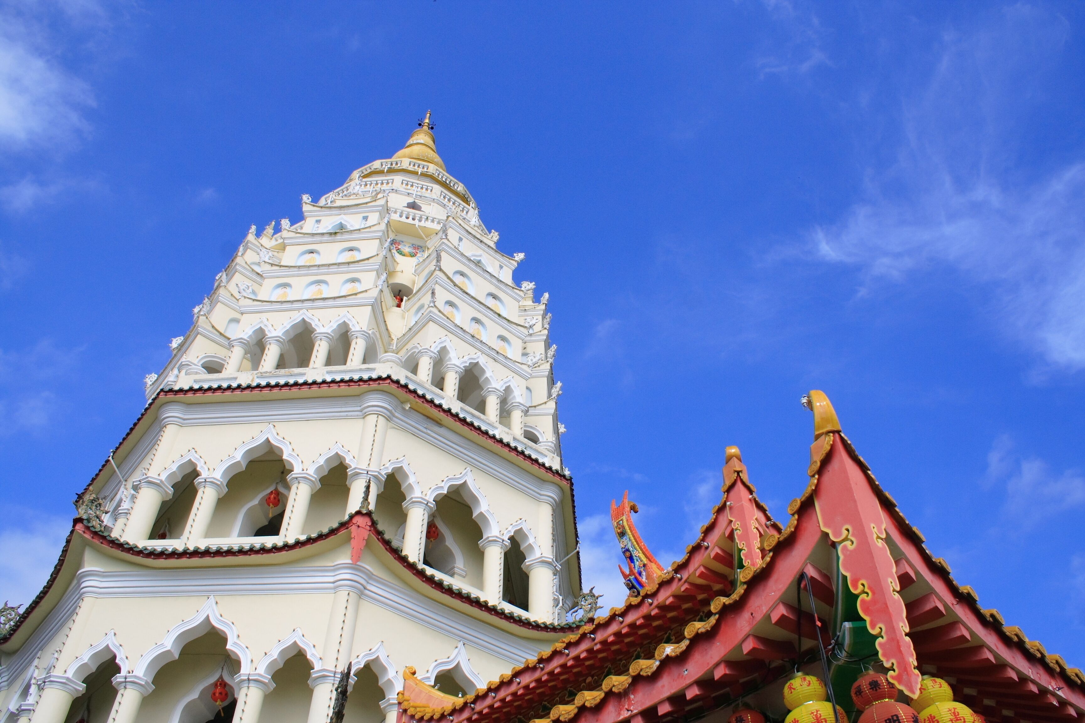 Um templo branco com uma agulha dourada e telhado vermelho contra um céu azul.
