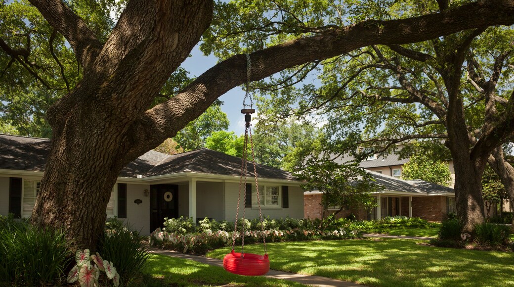 Red tire swing hanging from a tree at the detached residential house garden in Afton Oaks, Houston