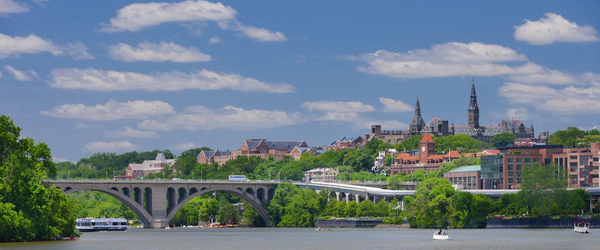 A river with a bridge, a clock tower, and a historic building with spires.