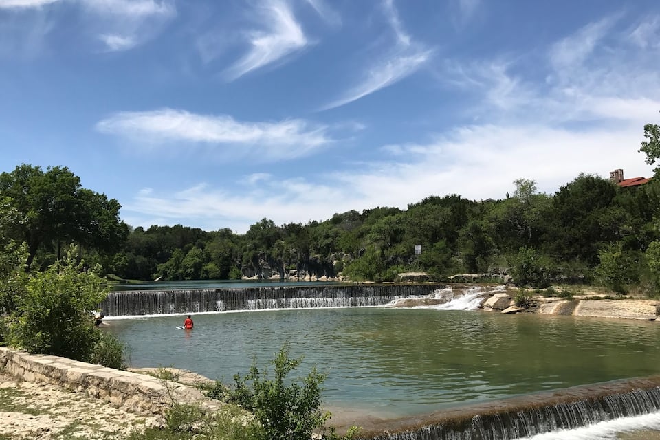 Una cascada que se precipita en un lago tranquilo rodeado de vegetación exuberante y un cielo azul despejado.