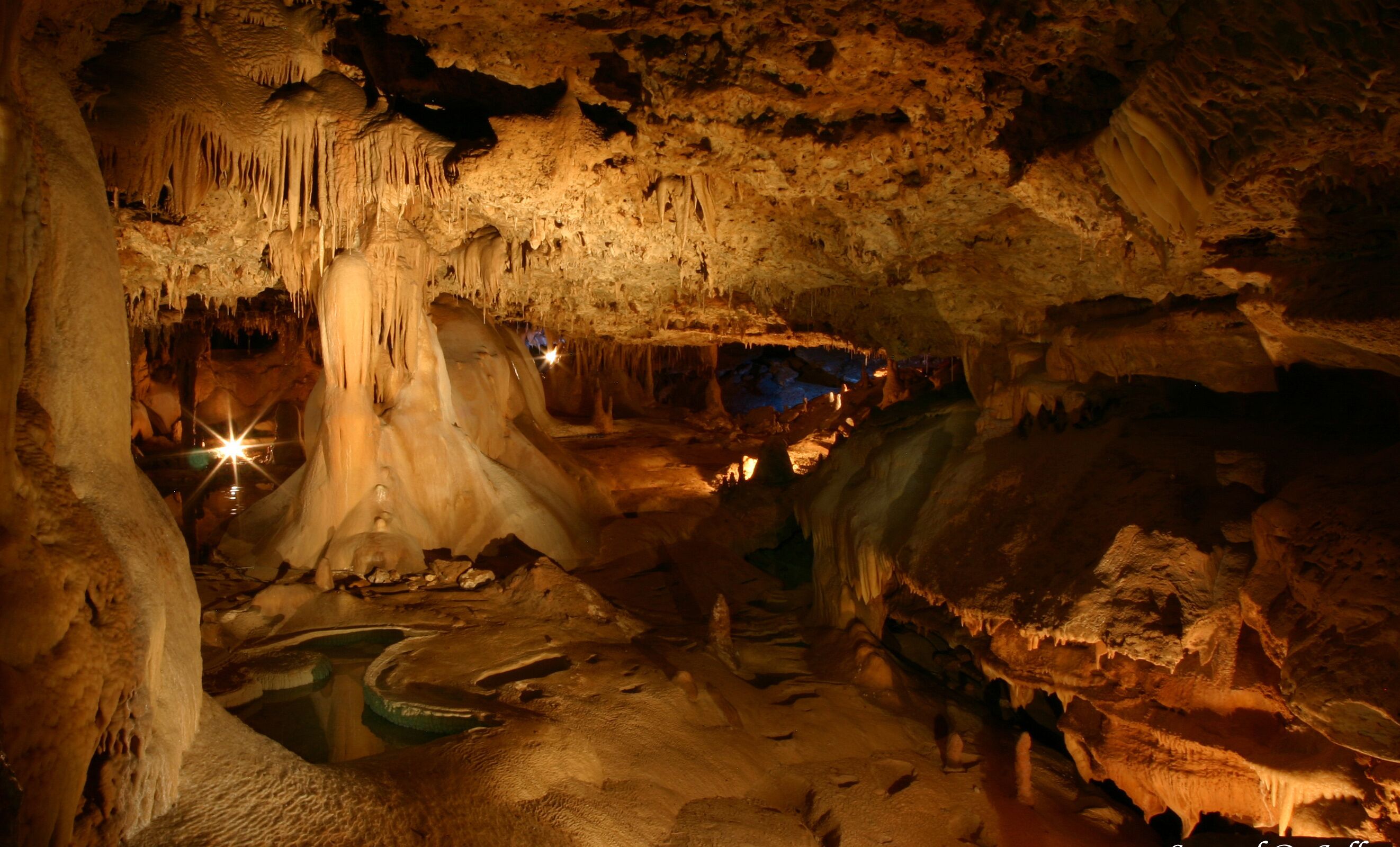 Cueva con estalactitas y estalagmitas, iluminada con luz artificial.