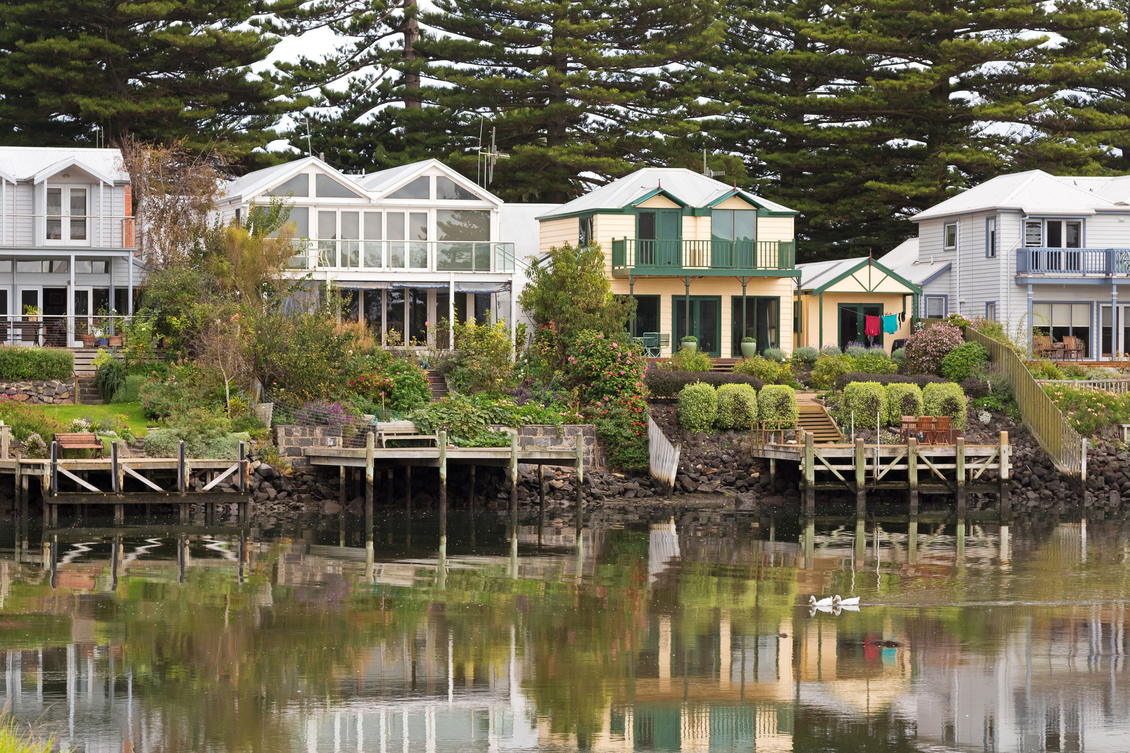 A row of waterfront houses with a dock, surrounded by lush greenery and a calm lake.