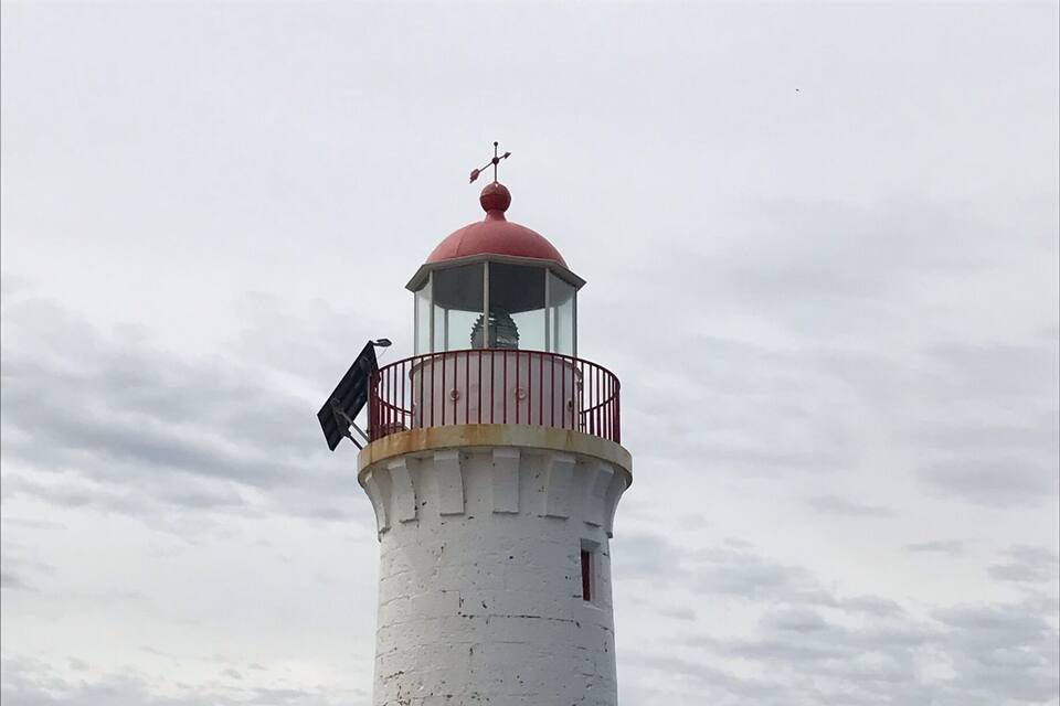 A white lighthouse with a red door and balcony, situated on rocky terrain by the sea.