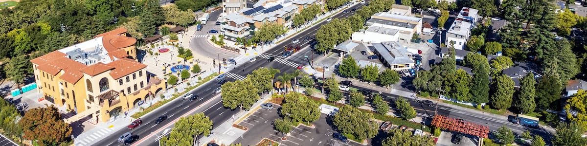Aerial view of commercial and residential areas of Menlo Park, California toward Palo Alto along El Camino Real Road near Middle Avenue. Backdrop distant San Francisco Bay and mountains