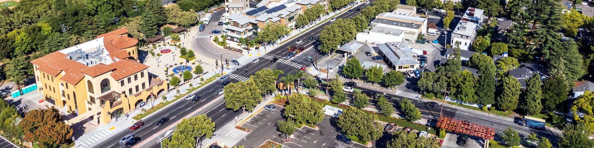 Aerial view of commercial and residential areas of Menlo Park, California toward Palo Alto along El Camino Real Road near Middle Avenue. Backdrop distant San Francisco Bay and mountains