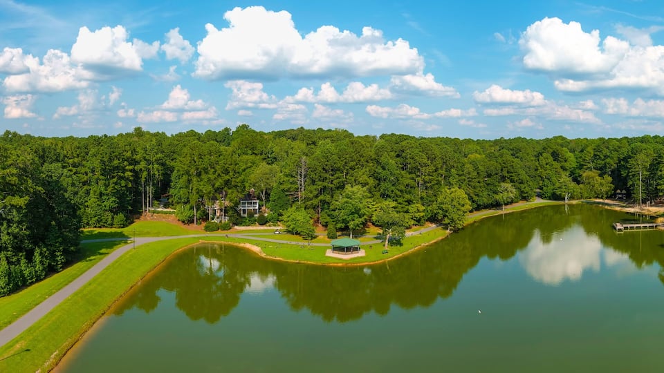 A lake surrounded by dense forest, a walking path, and a gazebo.
