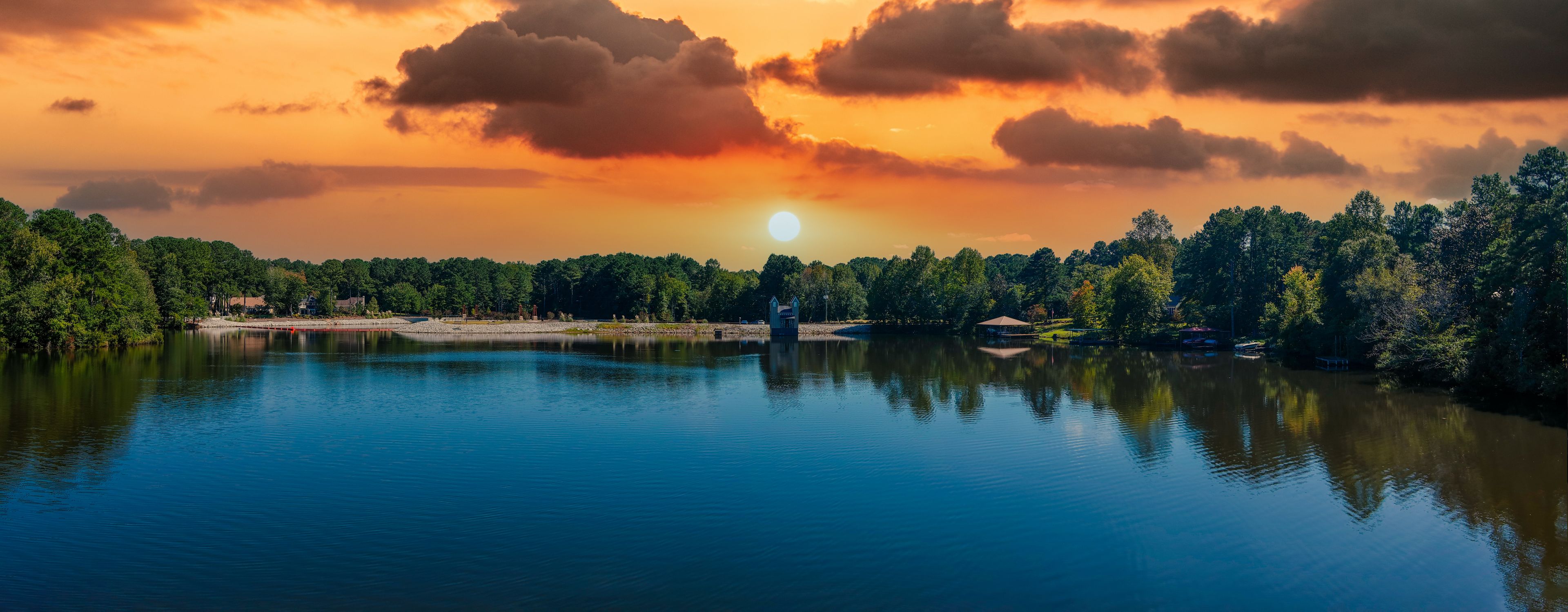 a stunning aerial panoramic shot of the blue waters of Lake Peachtree with vast miles of lush green trees and boats docked along the lake with powerful clouds at sunset in Peachtree City Georgia USA