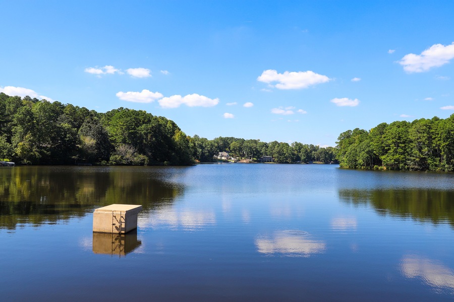 a gorgeous shot of vast still blue lake water surrounded by lush green and autumn colored trees with blue sky and clouds at Lake Peachtree in Peachtree City Georgia USA