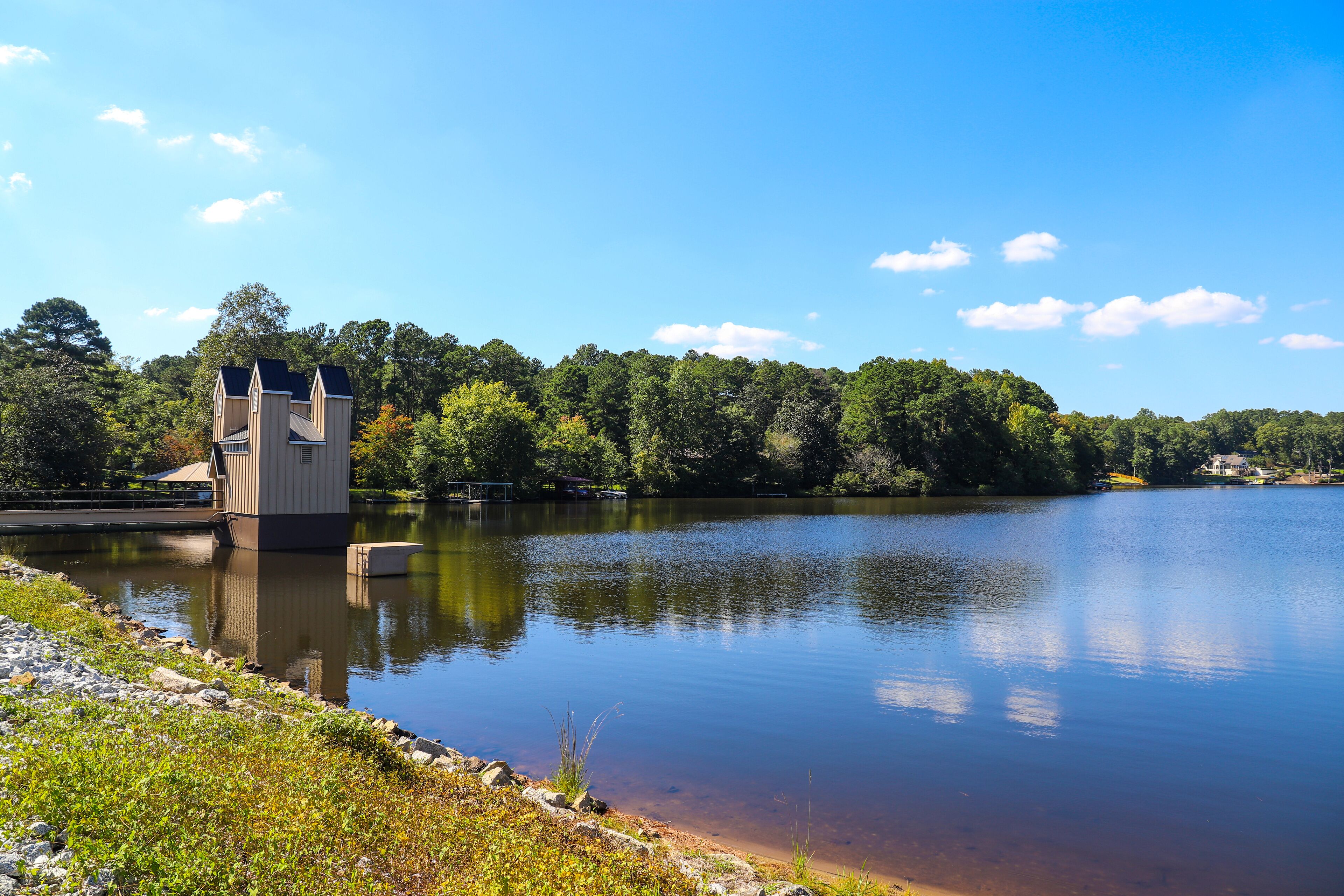 a stunning shot of the vast still blue lake water with lush green trees along the banks of the lake with blue sky and clouds at Lake Peachtree in Peachtree City Georgia