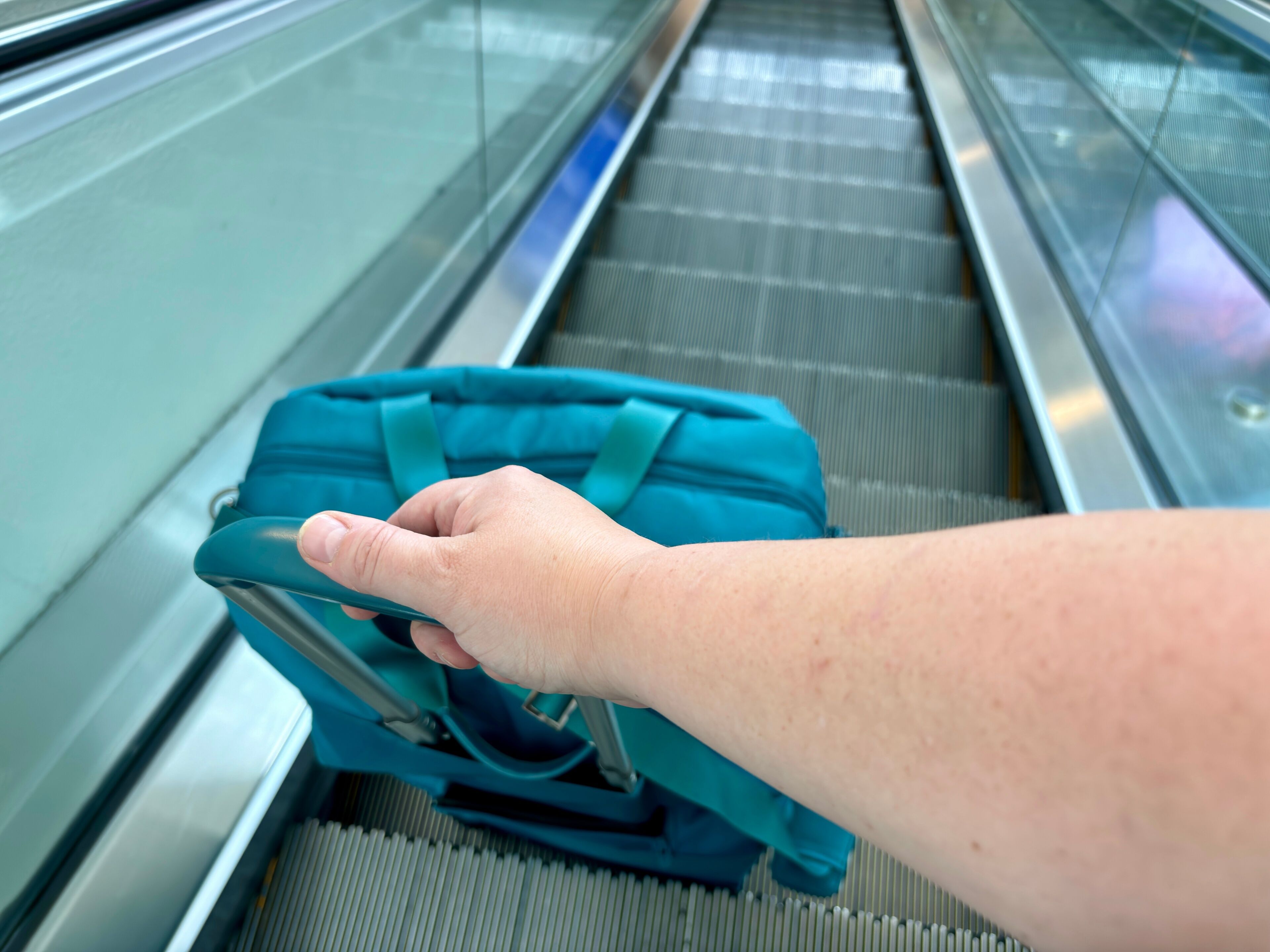 Hand and arm pulling teal suitcase on an escalator at CVG airport