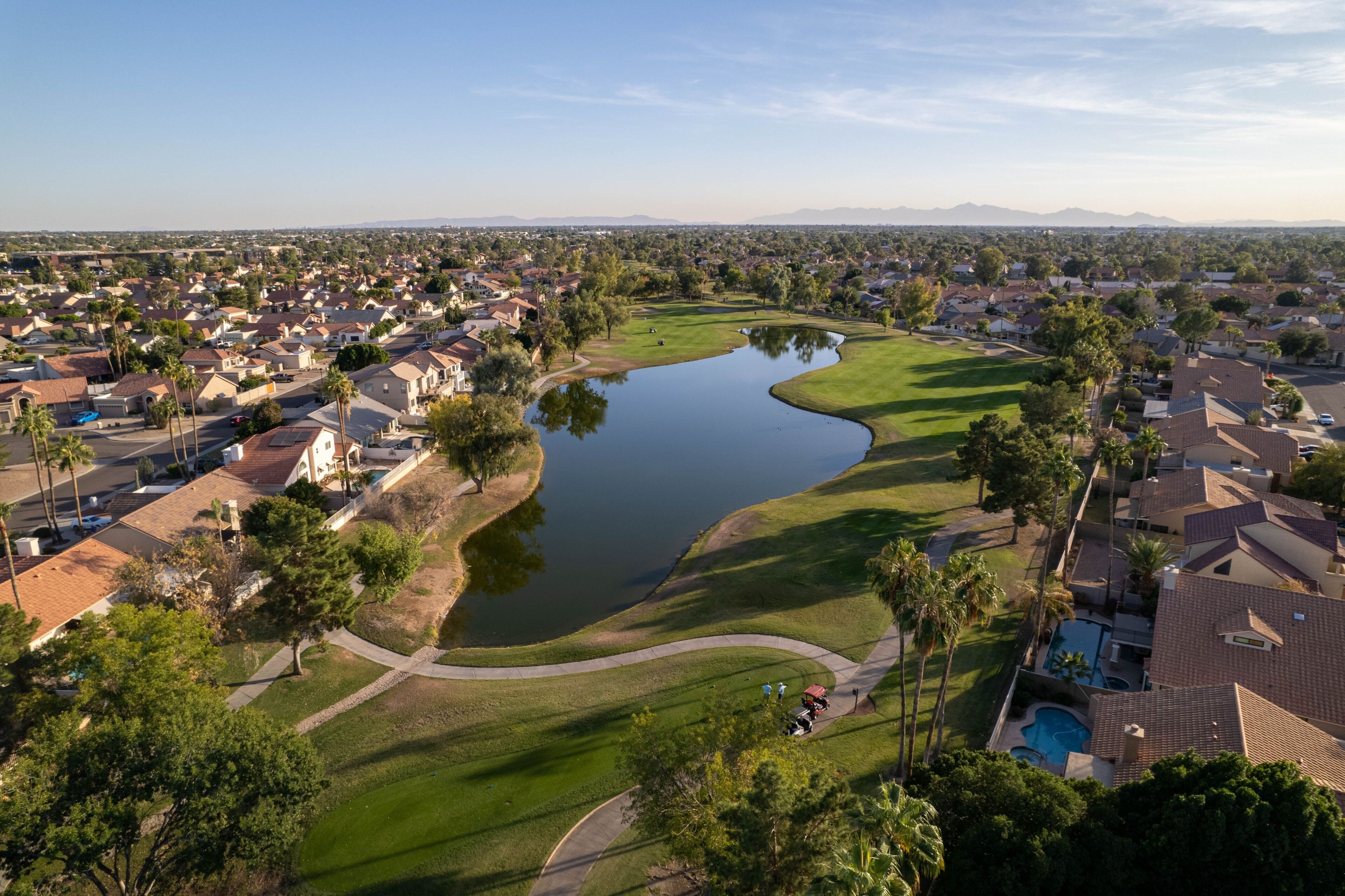 Un campo de golf con un estanque, rodeado de casas residenciales y palmeras.