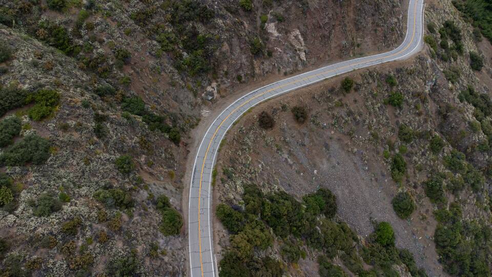 A winding mountain road with a guardrail, surrounded by rocky terrain and sparse vegetation.