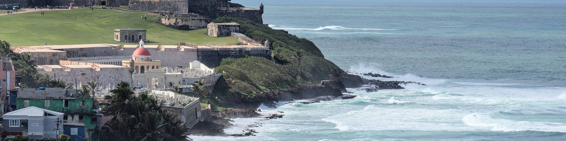 A coastal fortification with a lighthouse, a grassy area, and a rocky shoreline.