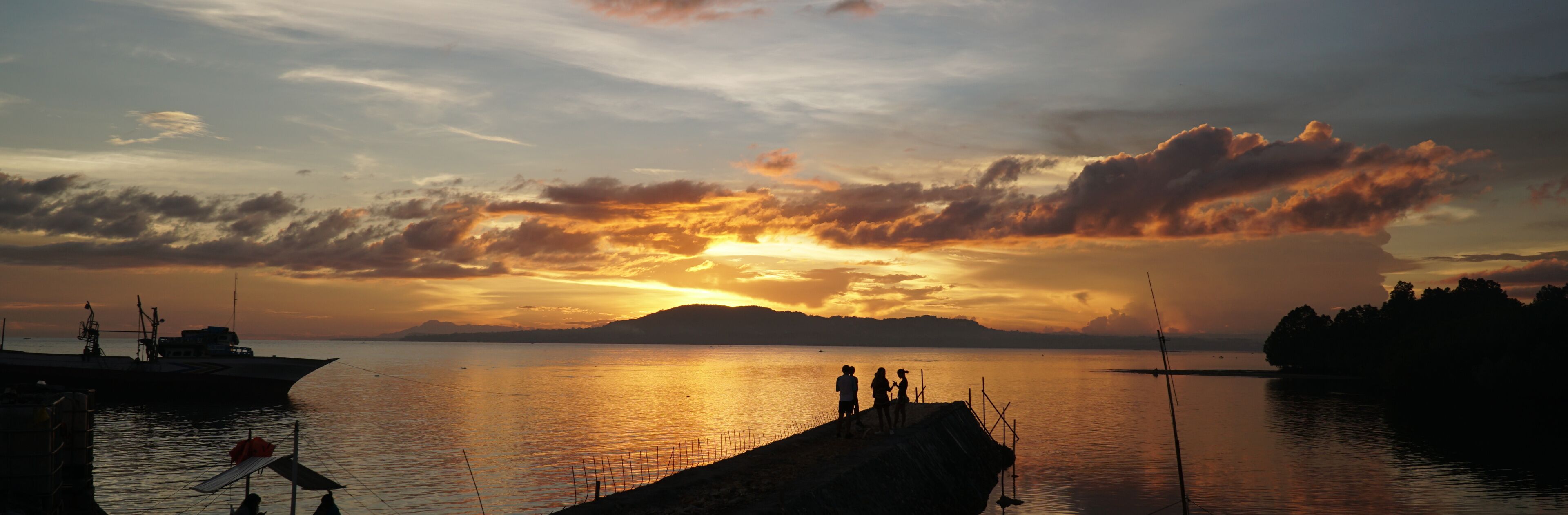 Um pôr do sol sobre um lago calmo, com barcos e um cais.