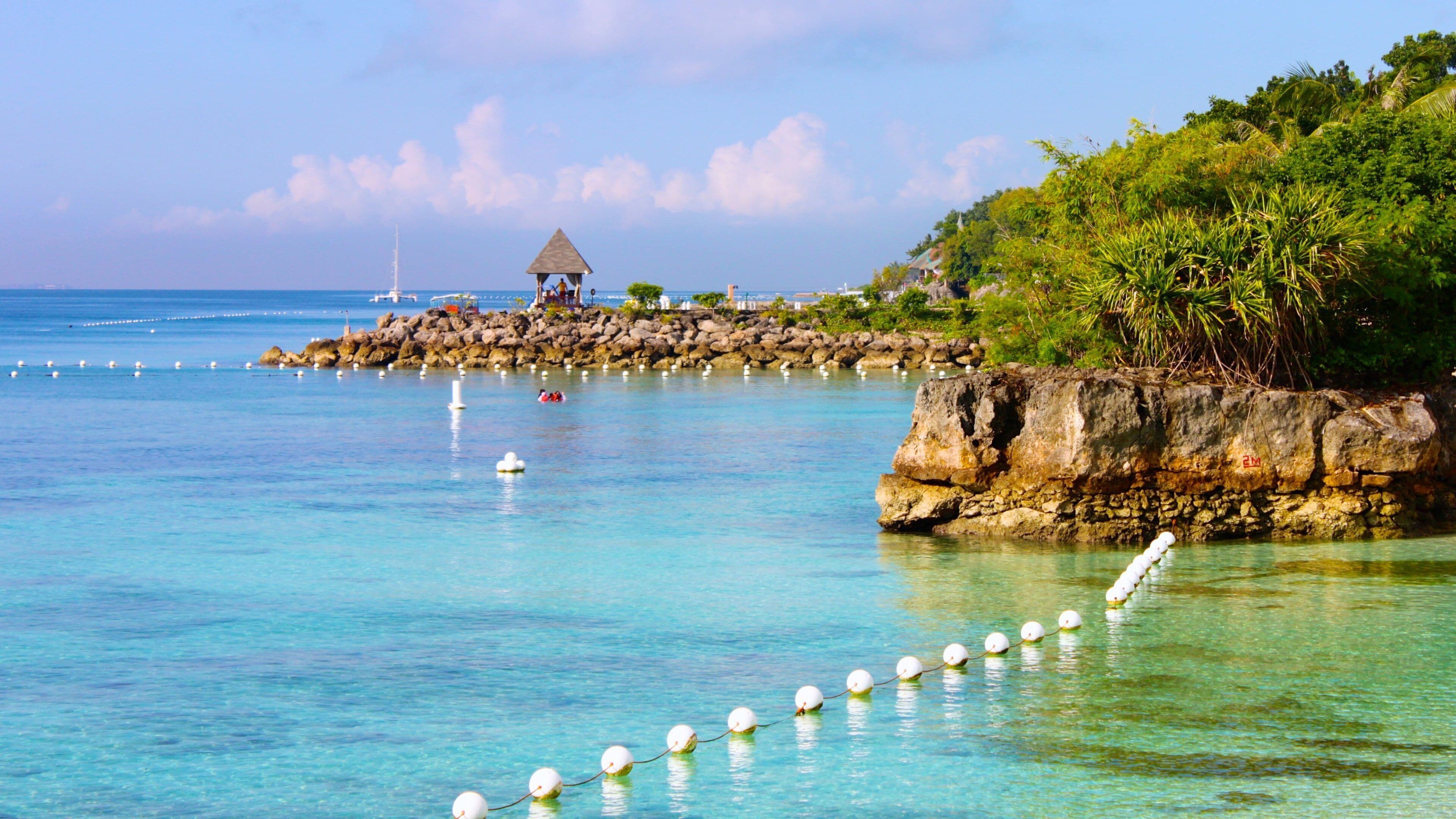 A tropical beach with clear turquoise water, a thatched-roof hut, and rocky outcrops.
